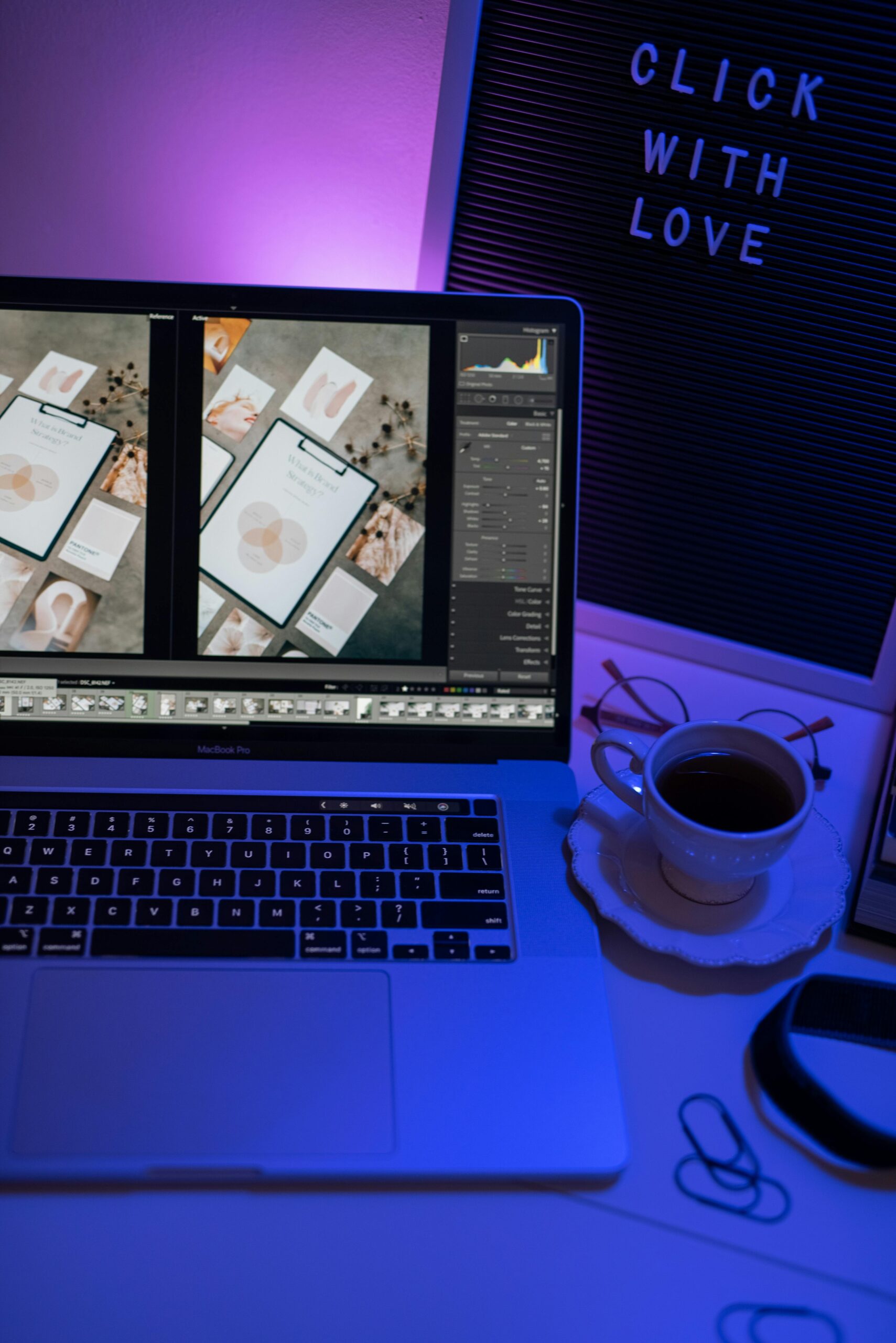 A cozy workspace setup featuring a laptop with photo editing software, lit by ambient purple light, and a cup of coffee.