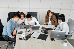 A diverse group of colleagues working together in an office setting with laptops and documents.